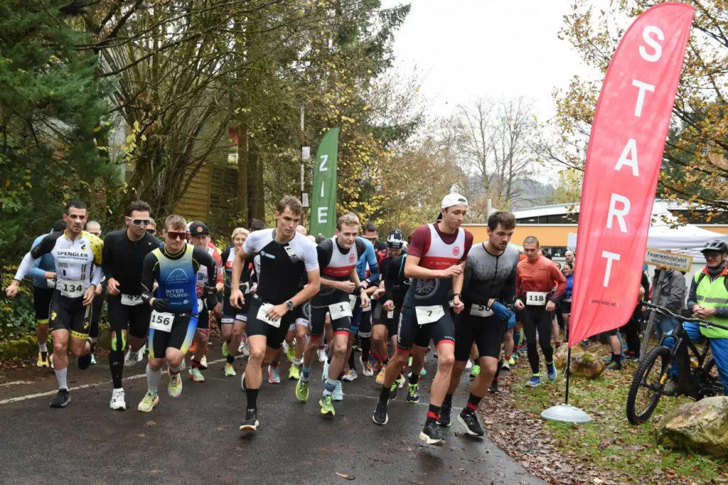 Startphase beim Lorsbacher Cross-Duathlon: zahlreiche Athleten laufen dicht gedrängt los, markiert durch Startbanner und Startfahnen in herbstlicher Waldumgebung.